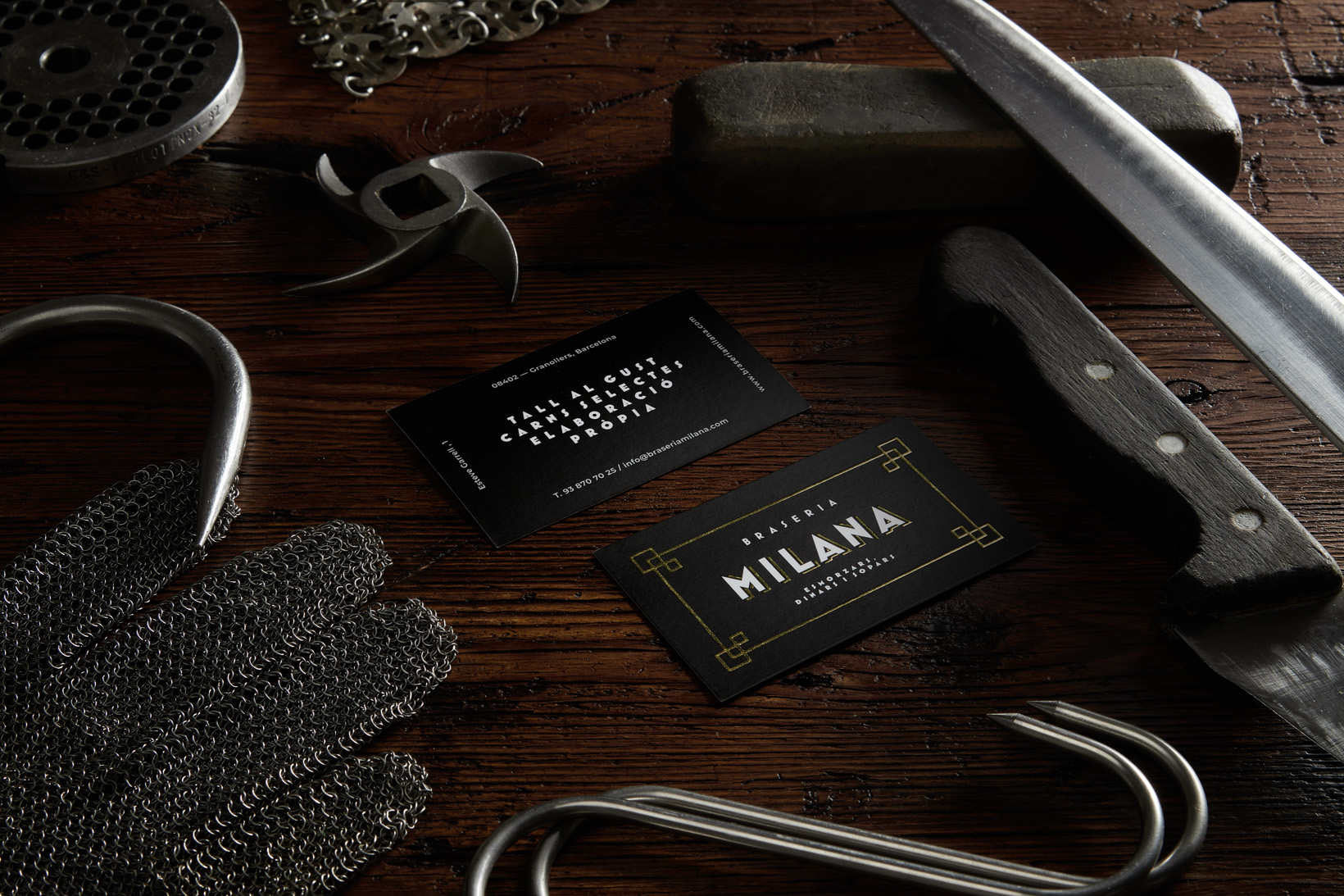 Business cards with new logo of restaurant grill Braseria La Milana next to butcher knives and iron gloves